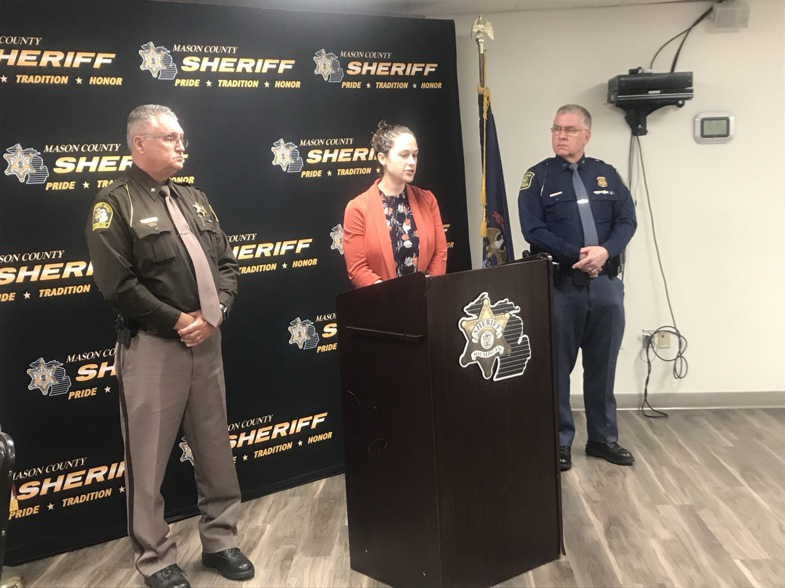 A sheriff, a prosecutor at a lectern and a state police lieutenant in front of a sheriff's office backdrop